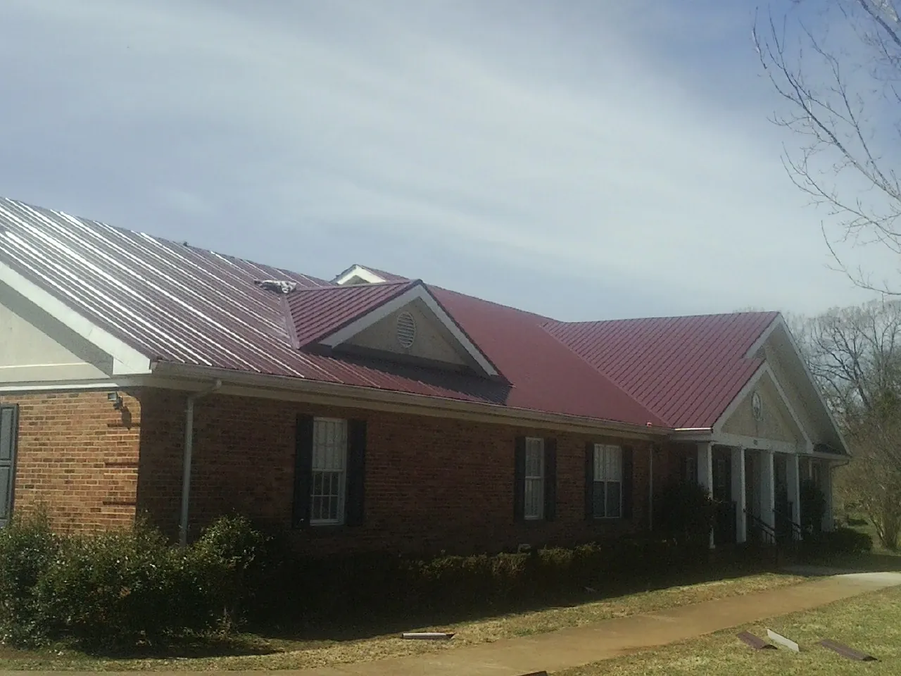 Red metal roof with gabled entries on a long brick building, from a Hail Damage Roof Repair job in Mc Dermitt