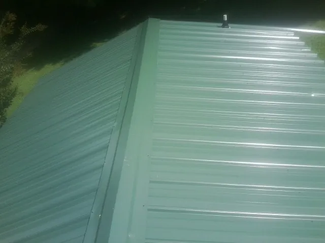 New green metal panels meeting at the ridge of a roof — Flat Roof Repair work by our crew in Mc Dermitt
