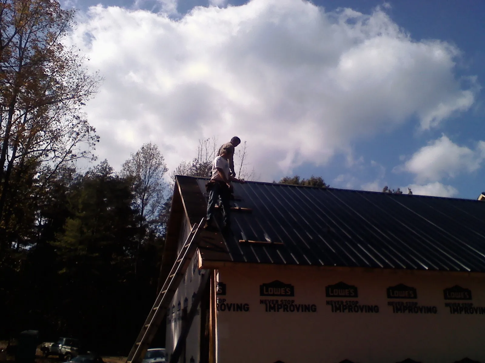 Roofer fastening dark metal panels high against a cloudy sky, from a Roof Inspection job in Mc Dermitt