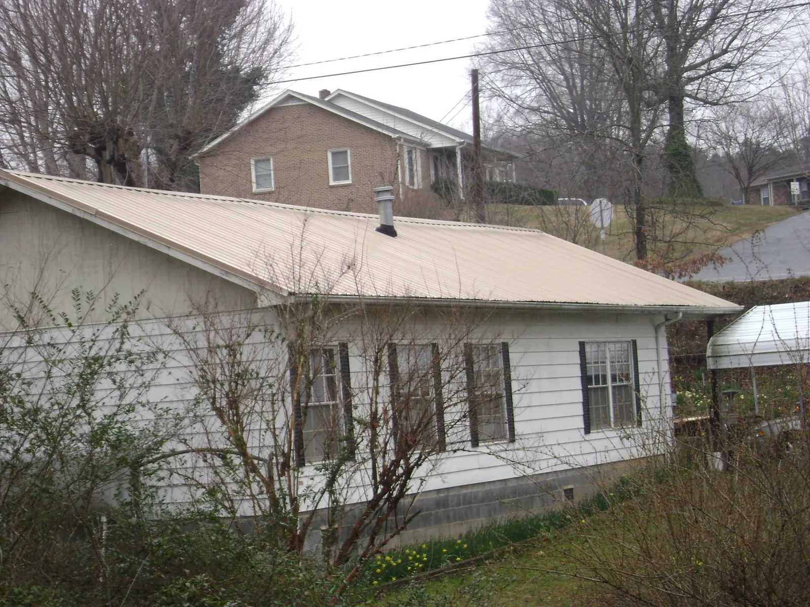 Tan metal roof on a white sided house set into a hillside — Commercial Roofing by Roofing Brothers in Mc Dermitt