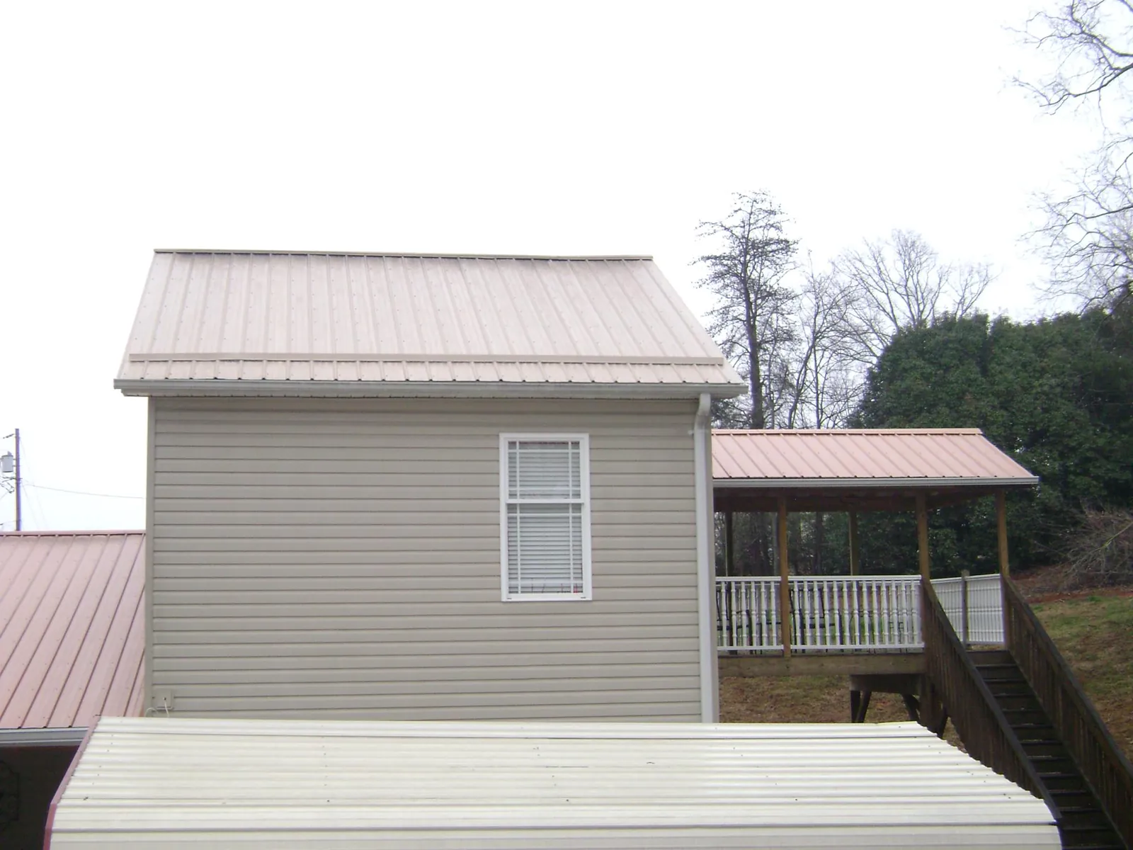 Tan metal roofs on a two story addition and attached porch, from a Roof Replacement job in Mc Dermitt